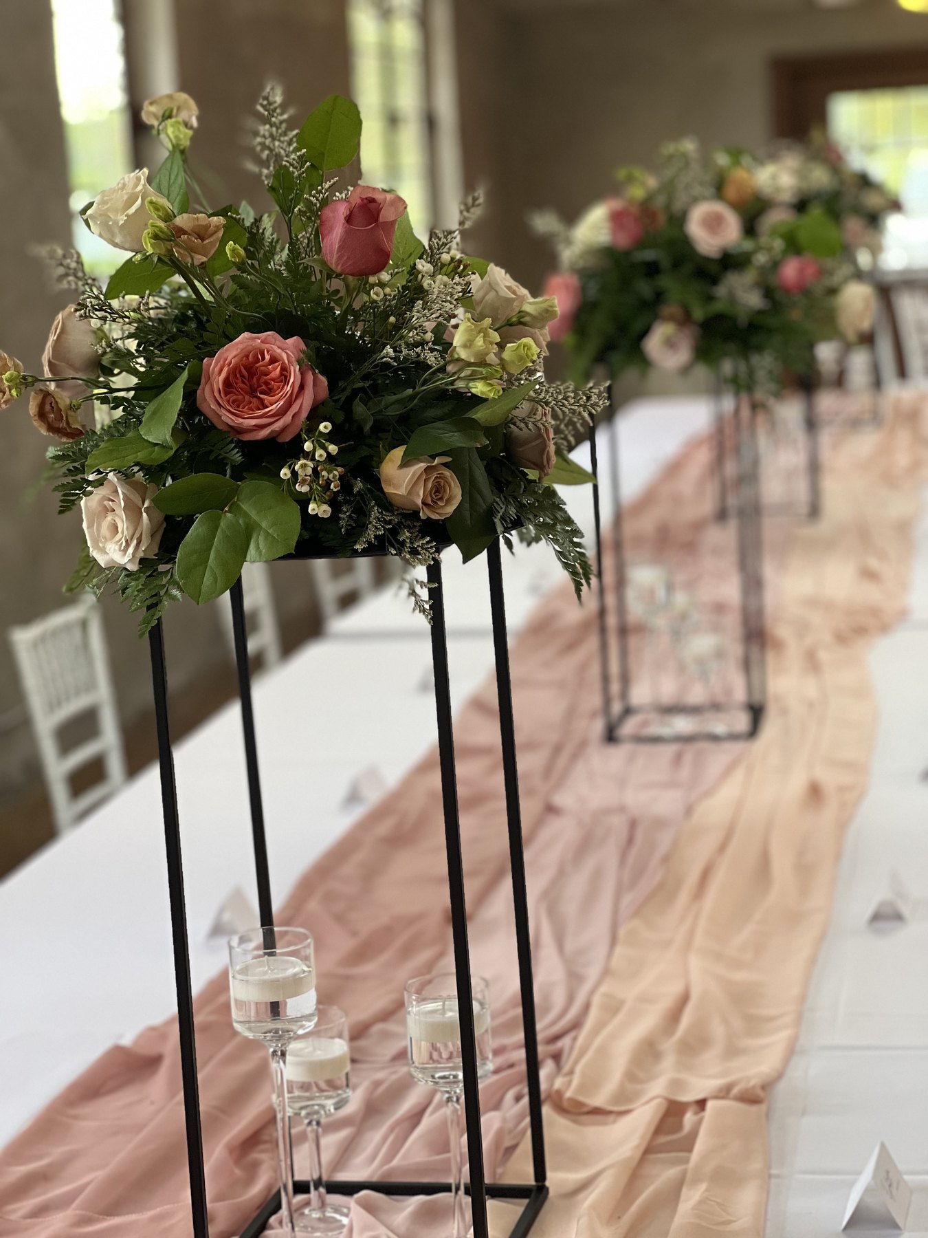 Tall floral arrangement beside blush event draping