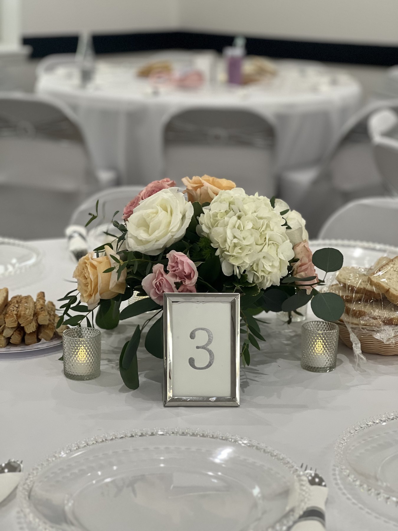 Table number with roses, hydrangeas, candles, and glassware